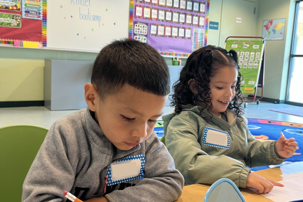 A young boy and a girl sit at a table and practice writing at Kinder Boot Camp.