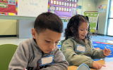 A young boy and a girl sit at a table and practice writing at Kinder Boot Camp.