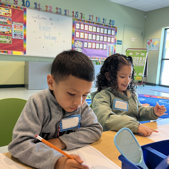 A young boy and a girl sit at a table and practice writing at Kinder Boot Camp.