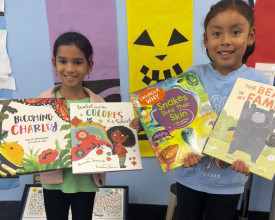 Two young girls are holding up books. 