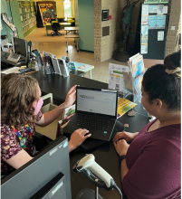 A photo of a library staff member checking out a laptop to a woman at the circulation desk at Cesar Chavez Library