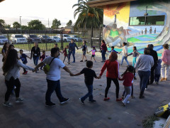 Parents and children holding hands in a large circle in the courtyard at César Chávez Library.