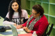 A volunteer assists a student working at a desk in a computer class.
